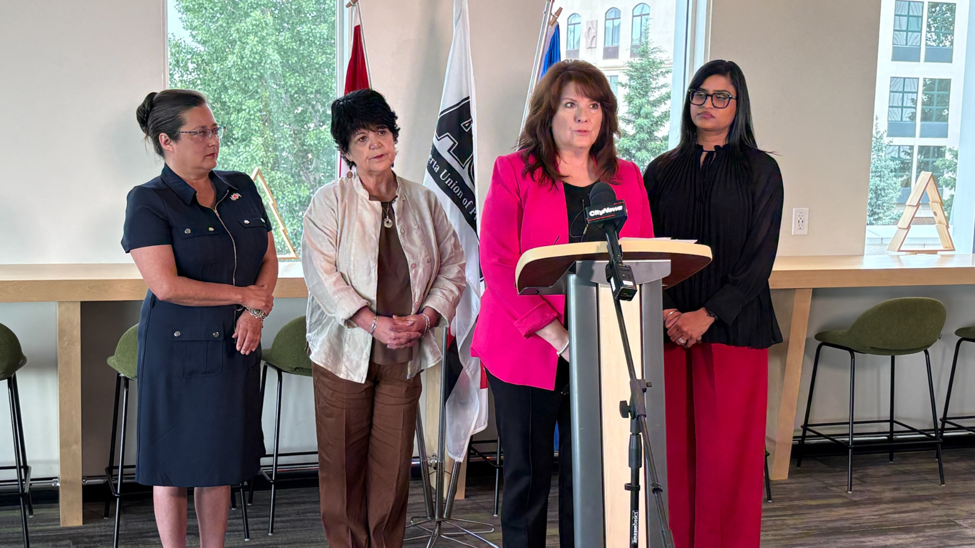 Leanne Alfaro, HSAA President, stands at a podium speaking with other labour leaders standing behind her.