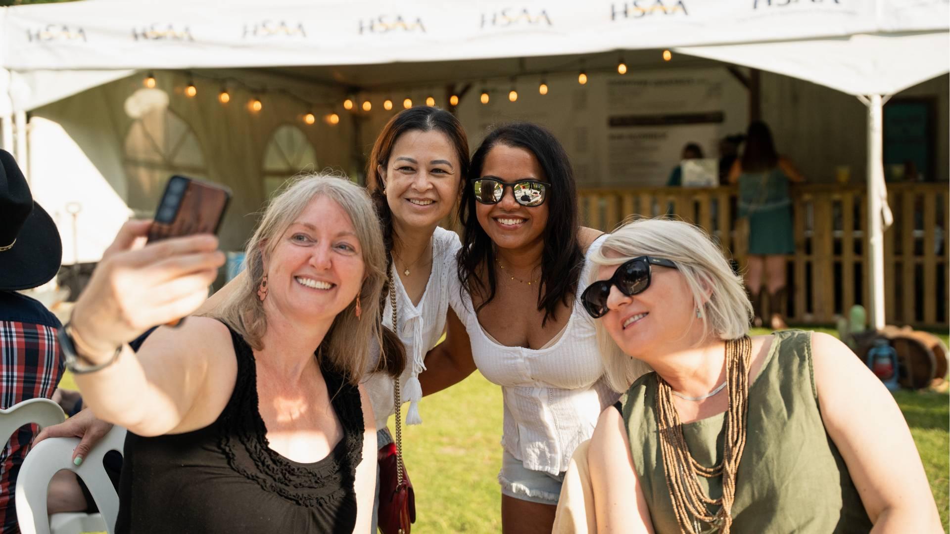 A group of four people taking a selfie in front of a event tent with the HSAA logo on it.