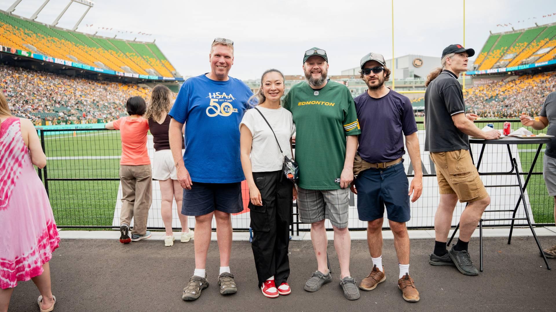 Four people standing for a photo in the end zone viewing area at an Edmonton Elks game