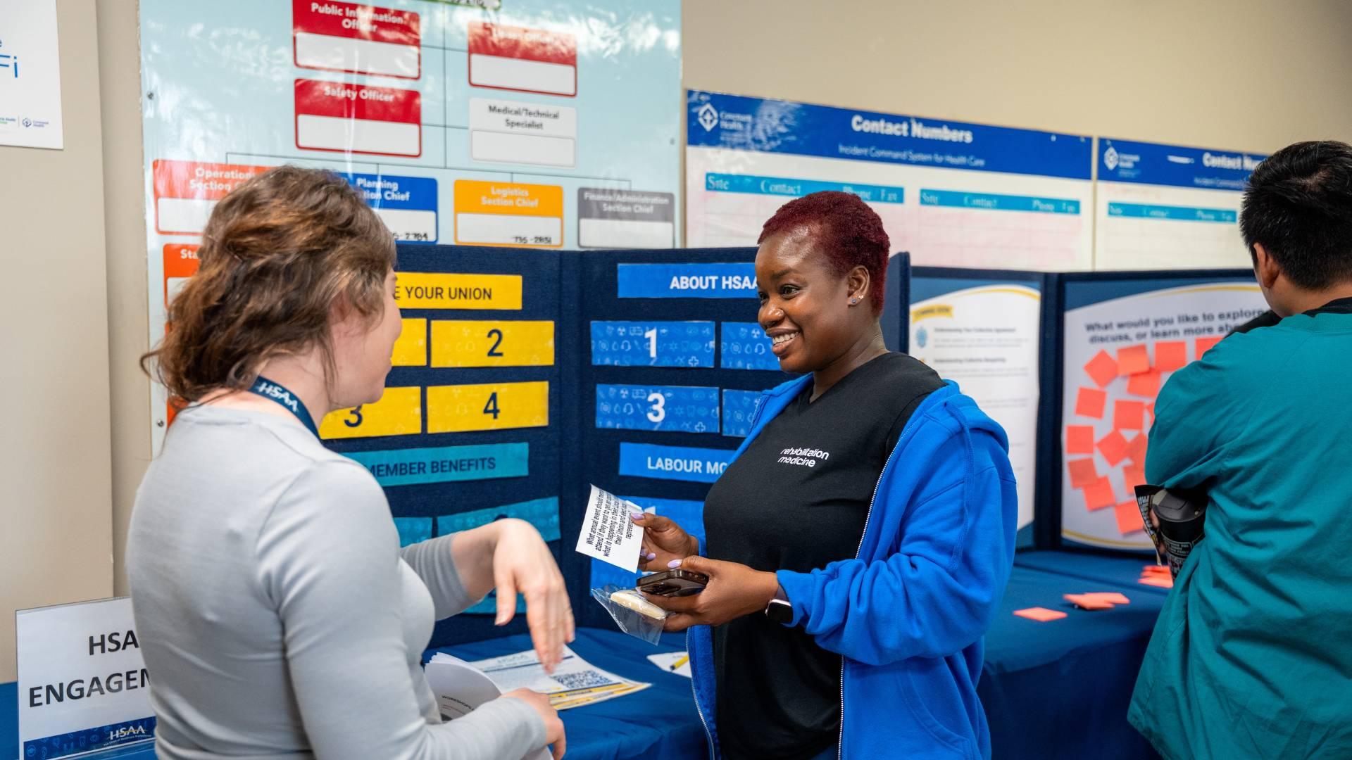 Two people talking in front of an HSAA display board.