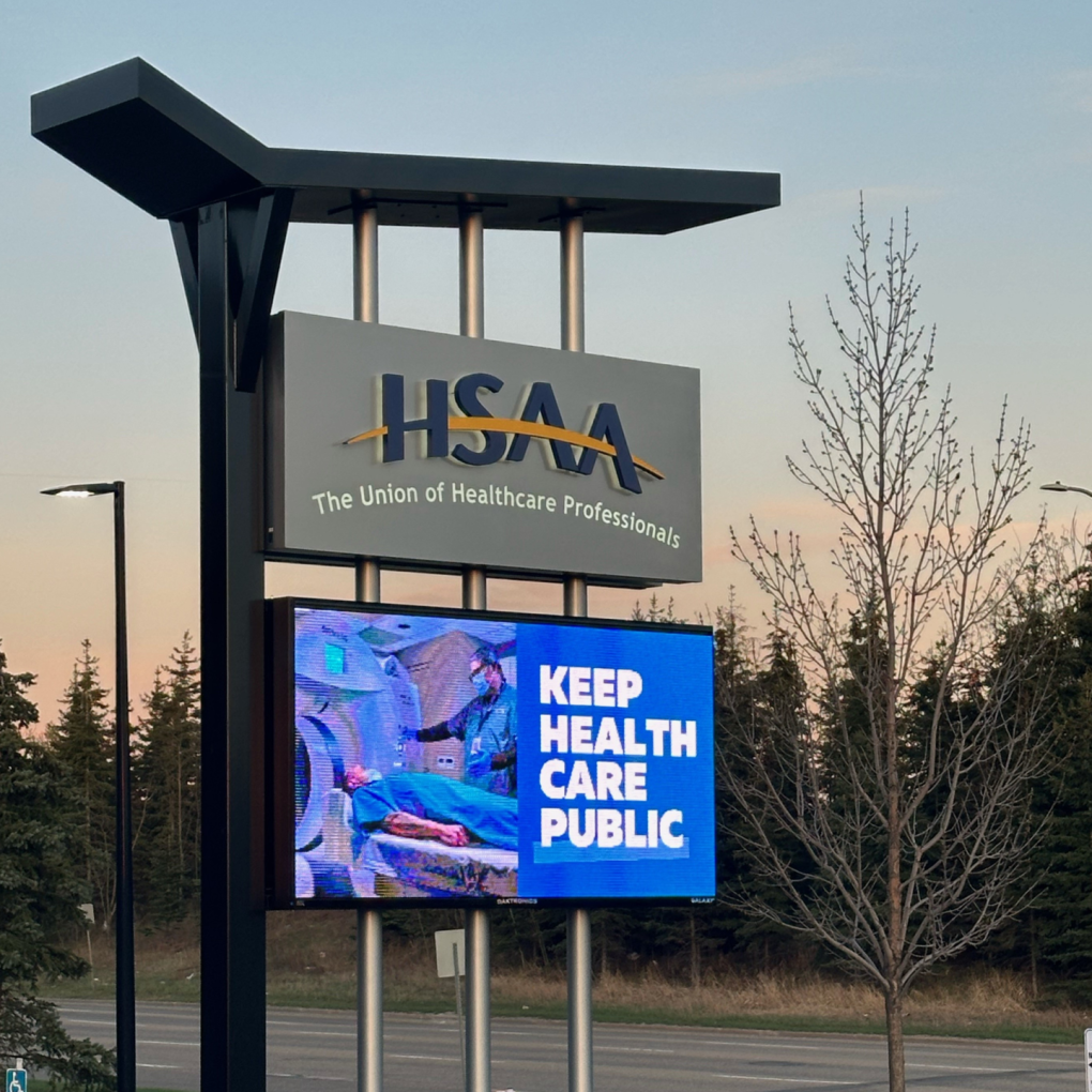 A sign outside the HSAA office with the logo and a digital screen that says "Keep Health Care Public"